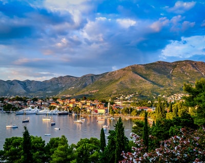 In the daytime, in the blue and white sky, surrounded by trees and the houses of the boats on the water near the mountain
